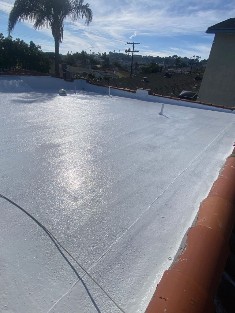 Fresh white silicone roof coating applied to a flat residential roof in Southern California, reflecting sunlight with nearby palm trees and neighborhood homes in the background.