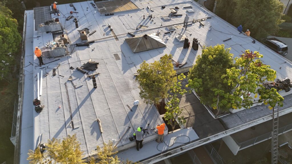Roofing crew installing and repairing a flat commercial roof with tools and materials spread across the rooftop while workers apply waterproofing layers and flashing.